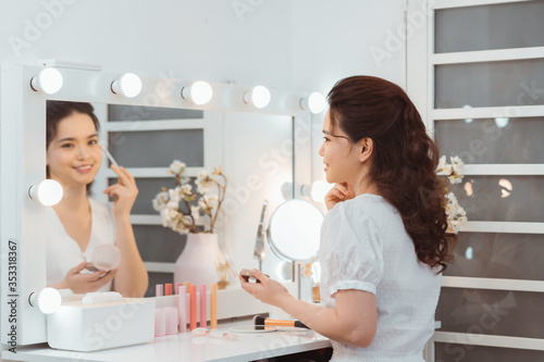 Papier peint Young stylish woman applying makeup by eye shadow brush in mirror