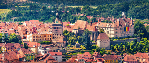 Panoramic morning cityscape of Sighisoara with Clock Tower and City Hall. Sunne summer view of medieval town of Transylvania, Romania, Europe. Traveling concept background.