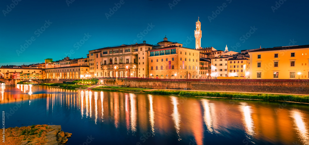 Panoramic evening cityscape of Florence with Old Palace (Palazzo Vecchio or Palazzo della Signoria) on background and Ponte Vecchio bridge over Arno river. Colorful night scene of Italy, Europe.