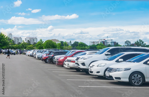 Car parking in large asphalt parking lot with trees  white cloud and blue sky background.