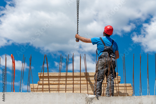 Construction worker holding a metal chain looking at the crane operator on the construction site