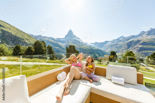 Mom with daughter relaxing in the rustic wooden terrace on mountain, alpine view