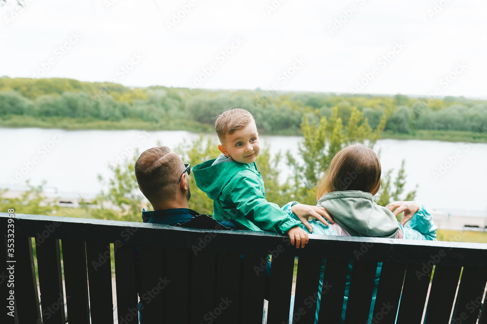 Family of three sitting on a bench in spring park, looking the lake. The little boy looks back.