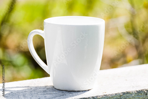 White coffee mug mock up outdoor with blurred background. Tea mug mockup for branding, template, logo, nature blurred background at summer terrace. White cup mock up, cappuccino mug mock-up outdoor. 