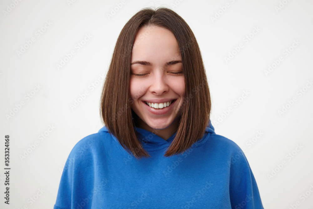 Pleasant looking young cheerful brown haired woman with bob haircut keeping her eyes closed while smiling happily, dressed in sporty clothes while posing over white background Pleasant looking young cheerful brown haired woman with bob haircut keeping her eyes closed while smiling happily, dressed in sporty clothes while posing over white background
