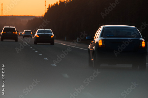 Sunset highway with cars on the country road. Evening orange sunset highway with multiple cars close up. Car trip with scenic road view, evening sun orange sunlight.