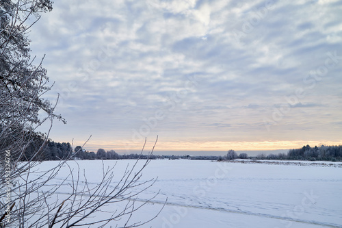 View from the shore of a river or lake, when the water is covered with ice powdered with snow. Morning or evening winter landscape