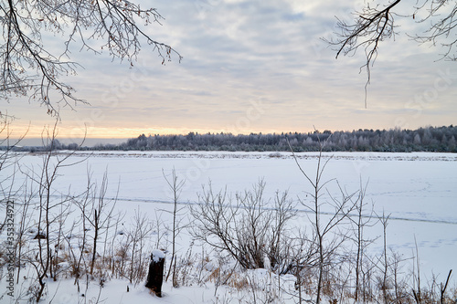 View from the shore of a river or lake, when the water is covered with ice powdered with snow. Morning or evening winter landscape photo