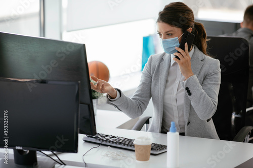 Beautiful businesswoman with medical mask working in office. Young businesswoman talking to the phone in office. 