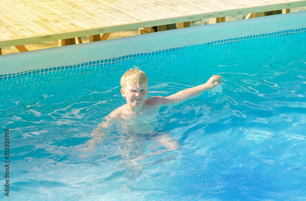 a strong blond boy with a smile swims in an outdoor pool. Child having fun in swimming pool. Summer vacation and healthy lifestyle concept