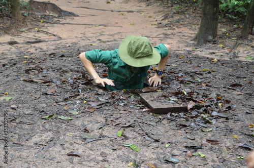 Man in Green Hat and Uniform Entering Hole to Cu Chi Tunnels in Vietnam