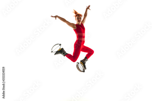 Beautiful redhead woman in a red sportswear jumping in a kangoo jumps shoes isolated on white studio background. Jumping high, active movement, action, fitness and wellness. Fit female model.