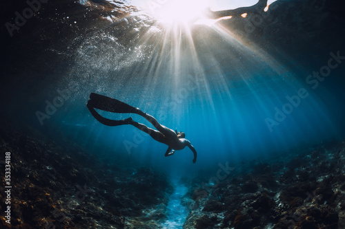 Fotografering Young freediver woman with fins glides and amazing sun rays