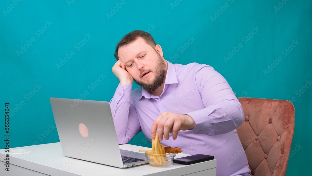 Male misses a laptop in the workplace and eats chips. Freelance concept, work at home, work fatigue, apathy Male misses a laptop in the workplace and eats chips. Freelance concept, work at home, work fatigue, apathy