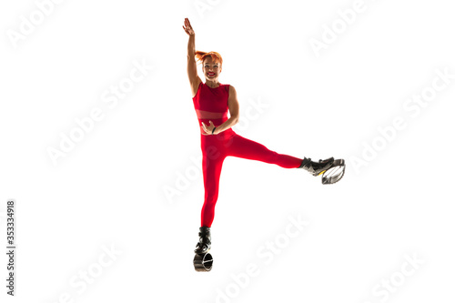 Beautiful redhead woman in a red sportswear jumping in a kangoo jumps shoes isolated on white studio background. Jumping high, active movement, action, fitness and wellness. Fit female model.