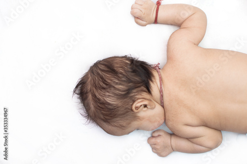 Small baby lying on a white bed sheet on his chest facing left with open hands © Tejjas