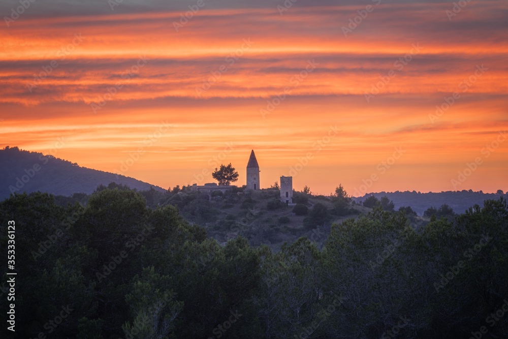 Spanish windmill on a hill surrounded by trees with a beautiful colourful sunset, Son Servera, near Cala Millor, Mallorca, Spain.