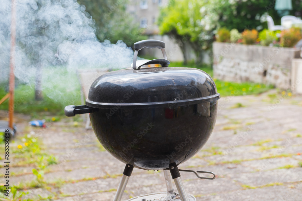 Outdoor black barbecue grill on a terrace. it is burning and smoke is coming out of it. Close up with a blurred background. Beautiful quality shot.