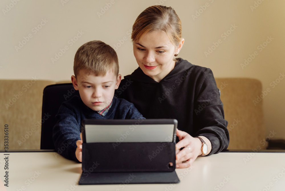 Mother using laptop and tablet teaching with her son online at home in his room Mother using laptop and tablet teaching with her son online at home in his room