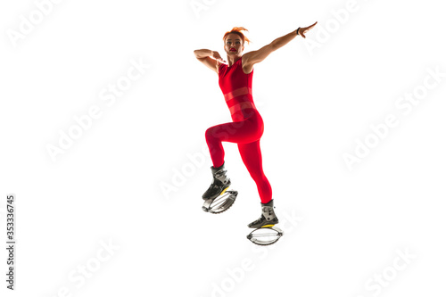 Beautiful redhead woman in a red sportswear jumping in a kangoo jumps shoes isolated on white studio background. Jumping high  active movement  action  fitness and wellness. Fit female model.