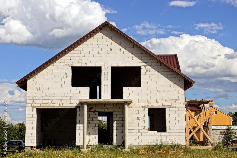large white unfinished brick private house with empty windows against the sky and clouds on a sunny day large white unfinished brick private house with empty windows against the sky and clouds on a sunny day