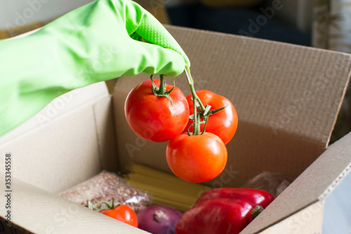Donation box. Food delivery during coronavirus. A girl in gloves takes food out of the box. Charity gathering of food during self-isolation.
