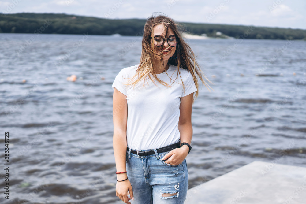 Portrait of a beautiful young woman in stylish glasses. Girl in white tshirt posing on the background of the lake landscape Portrait of a beautiful young woman in stylish glasses. Girl in white tshirt posing on the background of the lake landscape