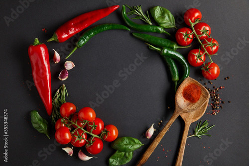 flat lay with red cherry tomatoes, garlic cloves, rosemary, peppercorns, basil leaves and green chili peppers on black