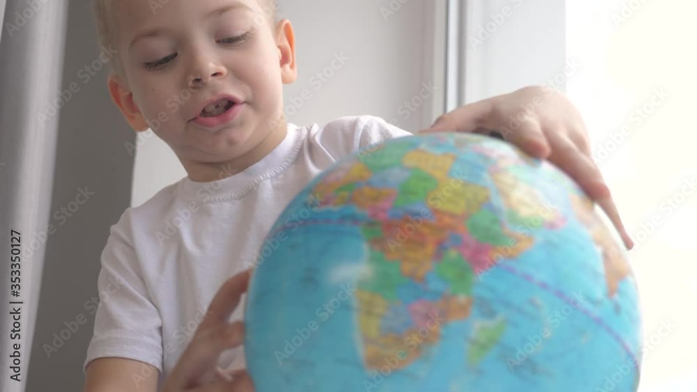 boy studies globe. lifestyle education travel tourism concept. child twists the globe sits on a window sill. kid looking for a country on a globe map. world map geography study boy studies globe. lifestyle education travel tourism concept. child twists the globe sits on a window sill. kid looking for a country on a globe map. world map geography study