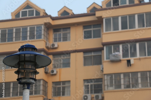 An old, rusted street lamp in front of a yellow apartment block building.