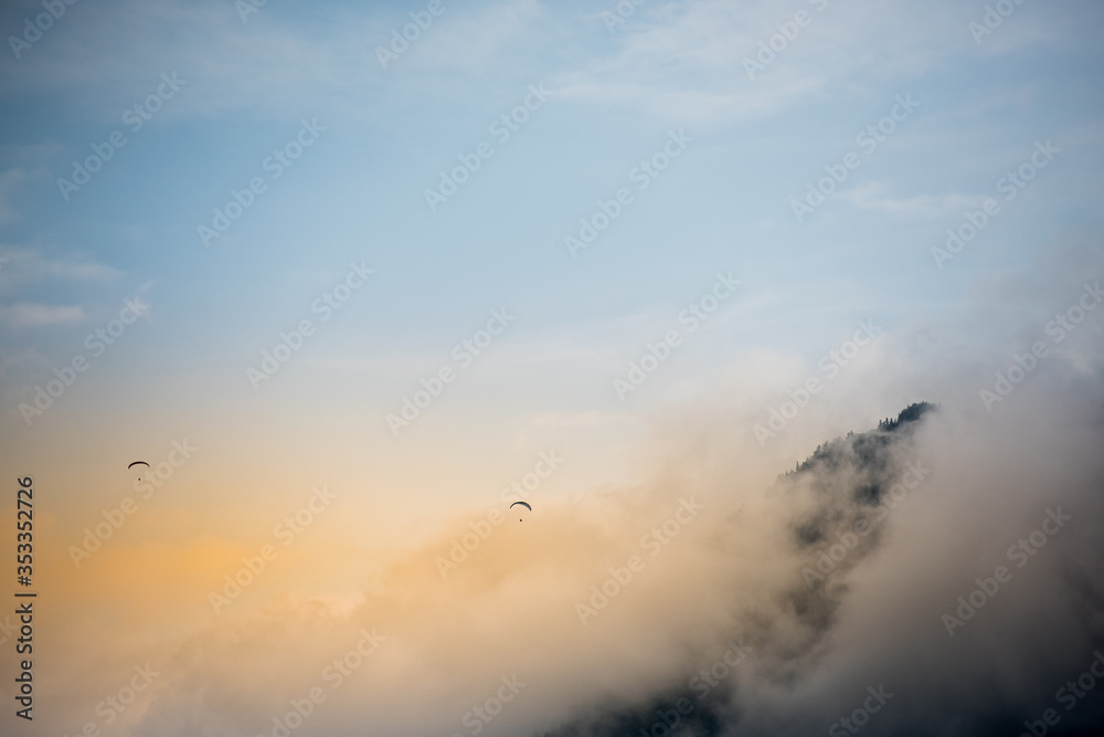 Paragliders flying over misty mountain range at dawn.