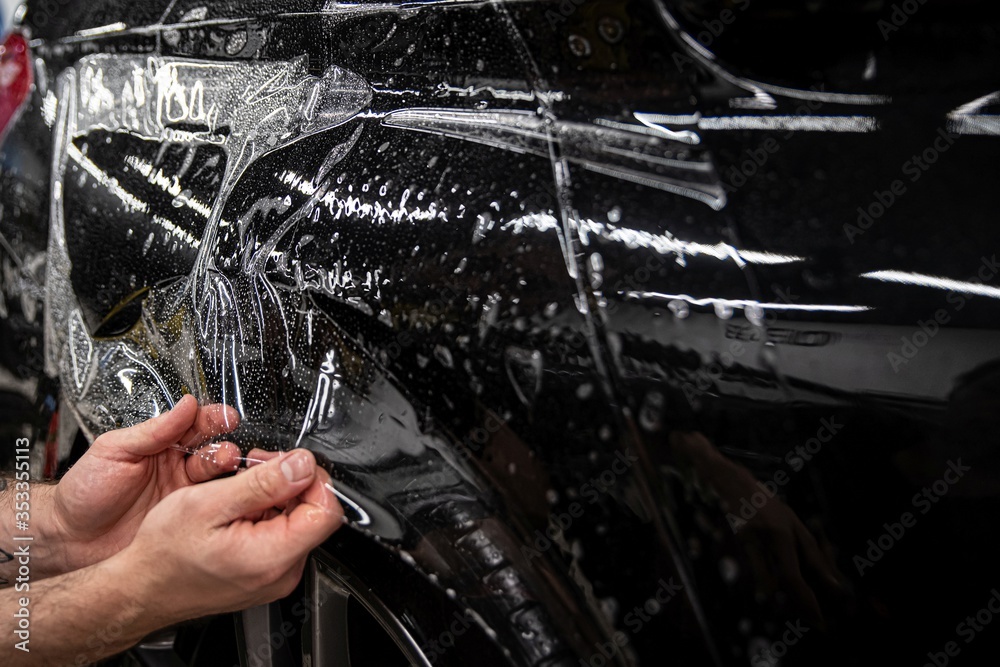 Car wrappping. Man car detailing studio worker appling transparent protection foil on car body.