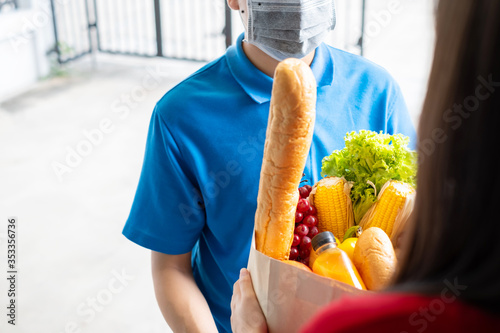 Food Delivery man wearing mask give fruit and vegetable shopping supermarket to receiver woman customer front house, express grocery service when crisis coronavirus, covid19 new normal lifestyle. photo