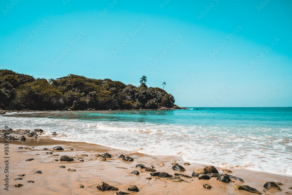 Beautiful secluded beach on an isolated island. Blue water and white waves spume on a sandy beach with stones in Sri Lanka. Escape to remote destination, relax and unwind near pleasant seashore.