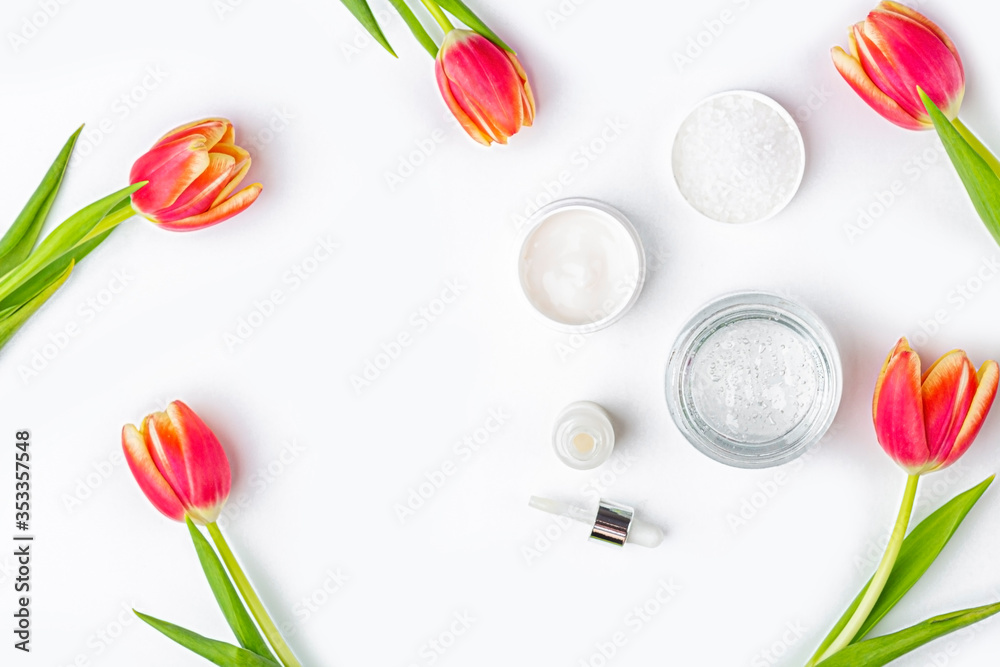Natural organic homemade cosmetics concept. Skin care, remedy and beauty products: containers with cream and serum among spring red tulip flowers on white background. Flat lay, copy space for text