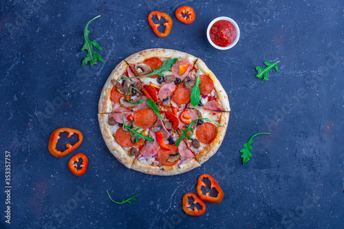 A fresh prepared pizza with salami, mushrooms, ham and cheese on a dark background. Italian traditional lunch or dinner. Fast food and street food concept. Flat ly, top view, copy space fot text