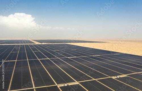 Aerial view of a landscape with photovoltaic solar panel farm generating sustainable renewable energy in a desert power plant in daylight.