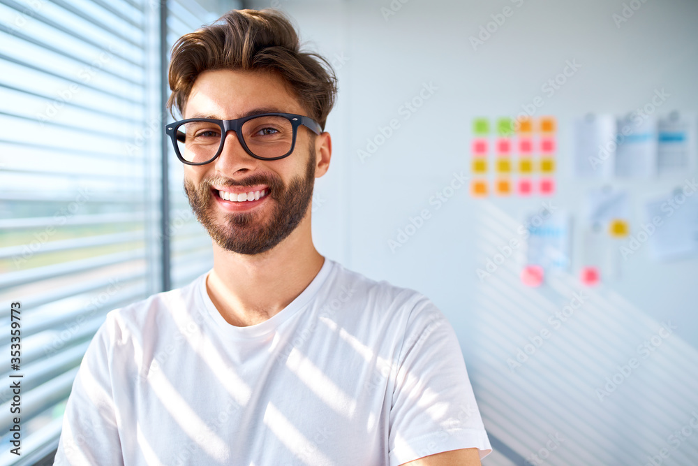 Portrait of casual young man standing in startup office. Looking at camera Portrait of casual young man standing in startup office. Looking at camera