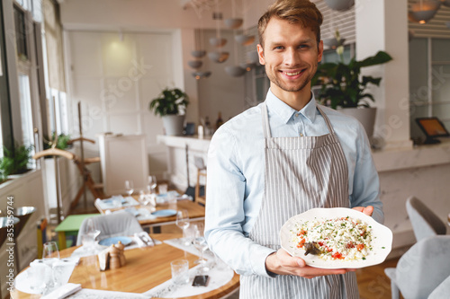 Cheerful young man holding plate of fresh salad