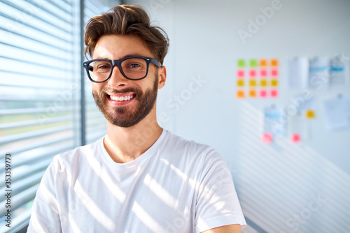 Portrait of casual young man standing in startup office. Looking at camera