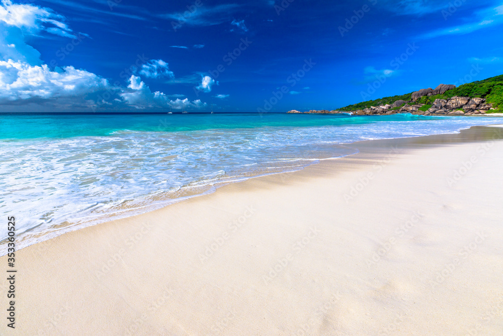 White sandy beach and turquoise clear sea of Grand Anse with copy space in the sand. Peaceful wallpaper of tropical Seychelles beach, La Digue.