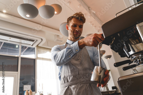 Smiling bartender in apron using professional coffee machine