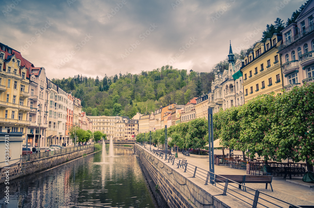 Karlovy Vary Carlsbad historical city centre, central embankment of Tepla river with fountains, colorful beautiful buildings, Slavkov Forest hills green trees background, West Bohemia, Czech Republic