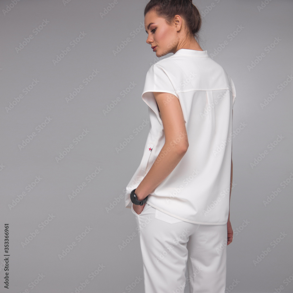 young stylish brunette nurse in white medical costume is standing from the back and looking away on the gray background. medical fashion concept, free space on left side young stylish brunette nurse in white medical costume is standing from the back and looking away on the gray background. medical fashion concept, free space on left side