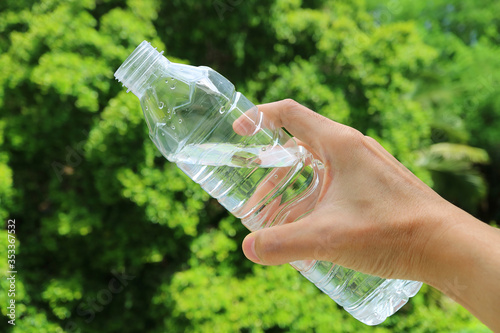 Hand holding a plastic bottle of drinking water against green foliage