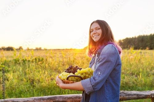 Young woman with basket of blue and green grapes, beautiful girl walking outdoor