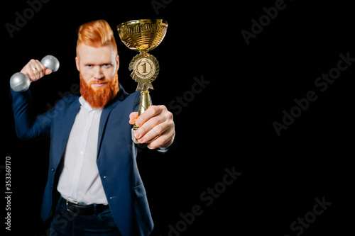 red-haired businessman holds a trophy on black background in studio, victory concept