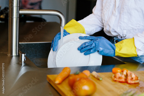 Detail of the hands of a person with gloves washing a plate with water in a kitchen