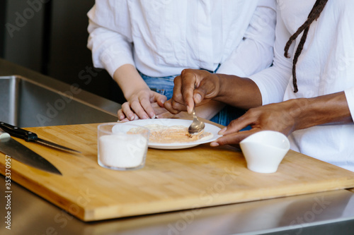 Detail of hands preparing a dish on a white plate on top of a wooden table with two knives