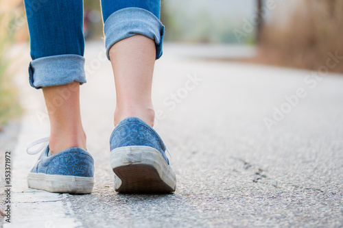 Walking women jeans and sneaker shoes on side road with grass flowers